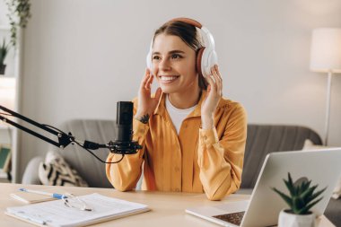 Evde çalışan genç bir kadın mikrofon ve dizüstü bilgisayar kullanarak podcast ses kaydı yapıyor. Podcast konsepti
