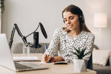 Canlı yayın sırasında kulaklık takan ve mikrofona konuşan bir kadın podcaster. Canlı, canlı konsept