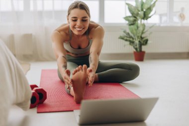 Gülümseyen sporcu kadın dizüstü bilgisayardaki beden eğitimi dersinden sonra evde egzersiz yapıyor, sağlıklı yaşam tarzının tadını çıkarıyor. Spor konsepti