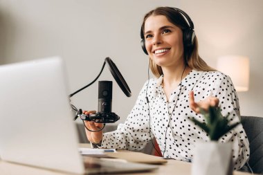 Genç bir kadın mikrofona konuşuyor ve evde ses yayını yapıyor. Çevrimiçi iletişim kavramı
