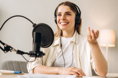 Genç bir kadın, stüdyosundaki bir podcast için ses kaydı yaparken mikrofona konuşuyor. Çevrimiçi teknoloji kavramı