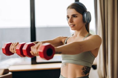 Genç bir kadın evde çalışırken halterleri kaldırıyor ve kulaklıkla müzik dinliyor. Eğitim kavramı