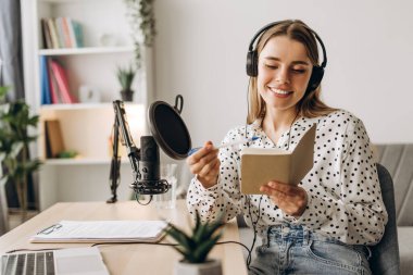 Evde çalışan genç bir kadın podcast bölümünden mikrofona konuşuyor ve not alıyor. Çevrimiçi iletişim kavramı