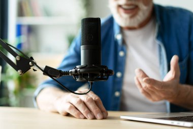 Gülümseyen olgun radyo sunucusu mikrofon kayıt podcast 'inde konuşuyor, kıdemli adam konuklarla uzaktan röportaj yapıyor iletişim için modern teknolojiler, yaratıcı iş, bulanık geçmiş