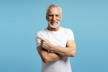 Kollarını çapraz yapıp gülümseyen yaşlı adam mavi arka planda izole edilmiş bir şekilde yüzünü yana çeviriyor. Reklam kavramı