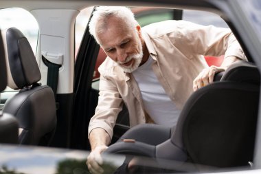 Üst düzey bir adam, aile seyahati sırasında torununun güvenliğini ve refahını ön planda tutmak ve gençler için güvenli bir yolculuk sağlamak için bir çocuk emniyet koltuğu kuruyor. Ulaşım kavramı