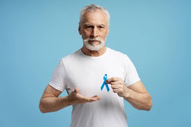 Mavi arka planda, prostat kanseri farkındalığı için mavi kurdele gösteren son sınıf öğrencisi. Sağlık hizmeti kavramı