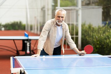 Mutlu kıdemli bir adam dışarıda pinpon oynayarak eğleniyor, aktif ve tatmin edici bir emeklilik yaşam tarzını kucaklıyor, aynı zamanda gülümsüyor ve diğerleriyle dostça bir rekabete girişiyor. Tenis konsepti