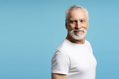 Gülümseyen son sınıf öğrencisi mavi arka plandan, fotokopi alanından modern stüdyoda izole edilmiş bir şekilde poz veriyor. Reklam kavramı