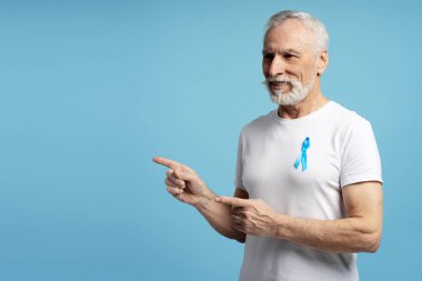 Üst düzey bir adam, mavi kurdele takmış, prostat kanseri farkındalığını destekliyor, stüdyo mavisi arka planda izole edilmiş. Sağlık hizmeti kavramı