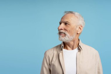 Beyaz sakallı, gülümseyen son sınıf öğrencisinin portresi, bej gömlek giyiyor ve mavi arka plana bakıyor, mutluluk ve pozitiflik saçıyor. Reklam kavramı