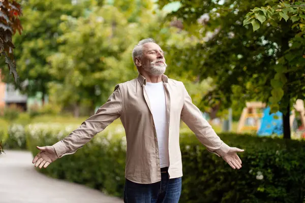 Gri saçlı sakallı bir adam parkta kollarını açmış, temiz hava soluyor ve özgürlüğün ve doğanın tadını çıkarıyor. Özgürlük kavramı