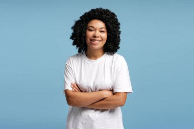 Mavi arka planda duran doğal kıvırcık saçlı neşeli Afro-Amerikan kadın. Yaşam tarzı, çeşitlilik ve duygu kavramı