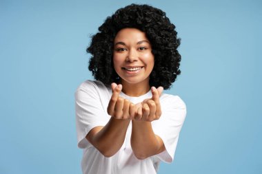Doğal kıvırcık saçlı, mutlu Afro-Amerikan kadın portresi. Maviye izole edilmiş parmaklarıyla küçük kalp hareketlerini gösteriyor. Kore sembolü, k popüler kültür kavramı