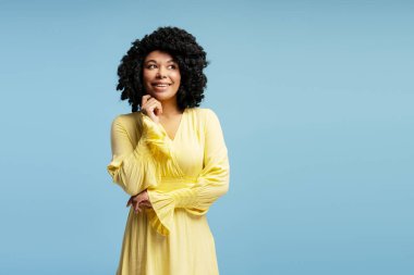 Çekici, kıvırcık saçlı, sarı elbiseli, düşünceli, mavi duvarın ötesini düşünen Afro-Amerikan kadın. Moda, güzellik, duygu konsepti