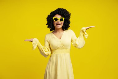 Gülümseyen, şık güneş gözlüğü takan, sarı elbise giyen, kameraya bakıp el ele tutuşan güzel Afrikalı Amerikalı kadının portresi. Moda, güzellik, duygu konsepti
