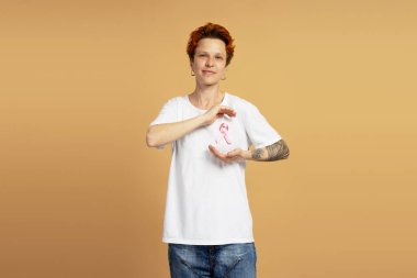 Pembe saçlı, beyaz tişörtlü ve göğüs kanseri için pembe kurdele takan genç insanların portakal rengi arka plana karşı farkındalığı.