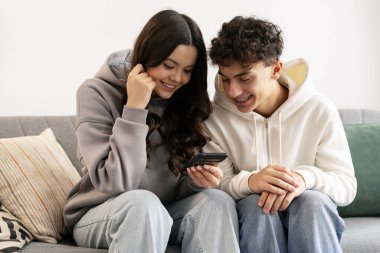 İki mutlu genç evde rahat bir kanepede oturup boş zamanlarının tadını çıkarırken akıllı telefon kullanıyorlar.