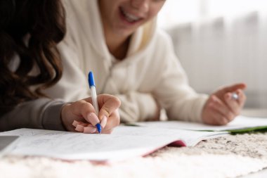 İki genç evde birlikte ders çalışıyor, ders kitaplarıyla çevrelenmiş bir şekilde not defterine notlar yazıyorlar, ödevleri üzerinde çalışıyorlar.