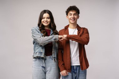 Bir hedefe ulaşmak için yumruk tokuşturan gülümseyen gençler, açık gri bir arka plana karşı sevinçlerini ve dostluklarını ifade ediyorlar.