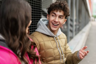 Diş teli takan genç bir adam bir okul molasında arkadaşıyla sohbet ediyor, şehirde kaygısız bir anın tadını çıkarıyor.