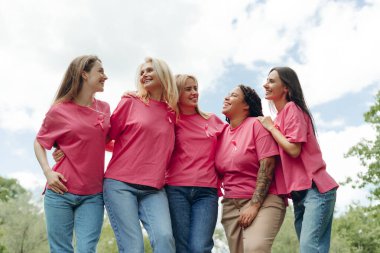 Pembe kurdeleli pembe tişörtler giyen beş neşeli kadın birbirlerine sarılıyor ve gülümsüyor, meme kanseri farkındalığını destekliyorlar. Destek konsepti