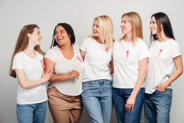 Farklı yaş ve etnik kökenlere sahip beş farklı kadın, gülümseyip kucaklaşırken pembe kurdeleli beyaz tişörtler giyiyorlar, meme kanseri farkındalığını ve birliğini kutluyorlar. Destek konsepti