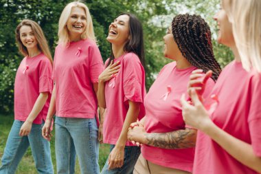 Pembe kurdeleli pembe tişörtler giyen bir grup neşeli kadın parkta birlikte yürüyor, meme kanseri farkındalığını destekliyorlar ve birlik ve umut gösteriyorlar.