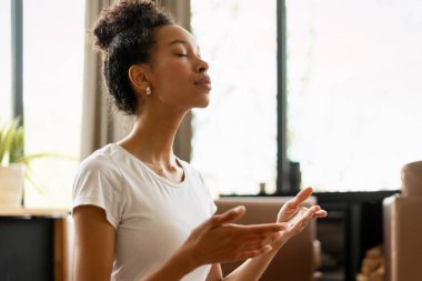 Huzurlu genç kadın evinde meditasyon yapıyor, zihinsel sağlığını geliştiriyor ve dengeli bir yaşam tarzı için farkındalığı kucaklıyor.