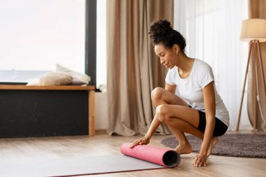 Sağlıklı ve aktif bir yaşam tarzını benimseyen, rahat oturma odasında canlandırıcı bir egzersizden sonra pembe yoga minderini yuvarlayan sağlıklı bir kadın.