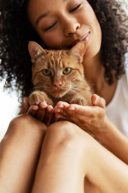 Sakin, genç bir kadın, kızıl kedisini nazikçe tutuyor, bir anlık şefkat ve arkadaşlığın tadını çıkarıyor.