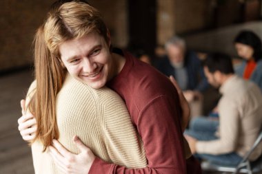 Mutlu genç adam grup terapisi sırasında bir kadına sarılıyor. Destek ve empati sunuyor.