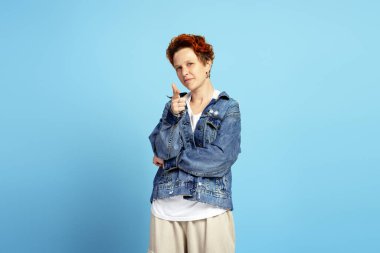 Stüdyoda mavi arka planda izole edilmiş, kameraya işaret eden, teşvikleri teşvik eden zarif genç bir kadın. Bireysellik, çeşitlilik ve kendini ifade etme kavramı