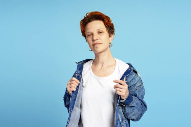 Kendine güvenen genç bir kadının portresi bireyselliği ve şehir tarzını ifade ediyor, mavi üzerine izole edilmiş kameraya bakıyor. Bireysellik, çeşitlilik ve kendini ifade etme kavramı