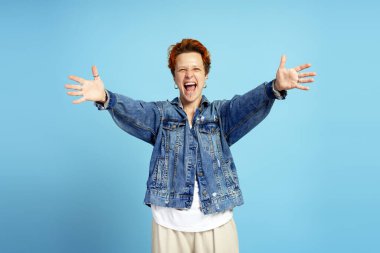 Neşeli, şık, genç bir kadın. Kollarını kaldırmış, rahat kot pantolon giyiyor ve mavi arka planda duruyor. Bireysellik, çeşitlilik ve kendini ifade etme kavramı