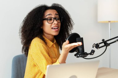 Genç bir kadın podcast yapıyor, profesyonel bir mikrofon kurulumuna hitap ediyor, modern iletişim ve medya becerilerini sergiliyor