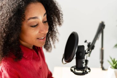 Genç bir kadın kendi stüdyosunda podcast yaparken mikrofona konuşuyor, yaratıcılığını ve medyaya olan tutkusunu gösteriyor.