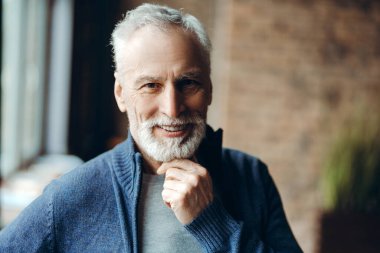 Beyaz saçlı, sakallı, zarif, gülümseyen bir son sınıf öğrencisinin portresi. Kapalı mavi bir süveter içinde, kendine güveni ve mutluluğu yayarak çenesine dokunuyor.