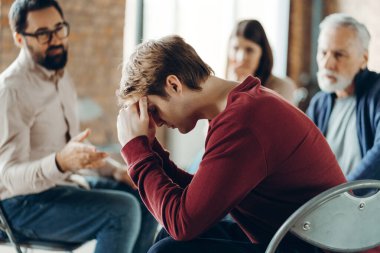 Terapi seansı sırasında depresyonda olan bir adam terapist ve diğer hastalarla el ele tutuşup zihinsel sağlık sorunlarını tartışıyor. Ruh sağlığı konsepti