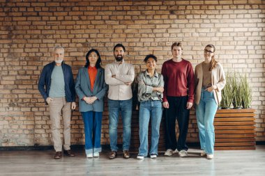 Farklı yaş ve etnik kökenlere sahip gülümseyen çok uluslu iş adamları, modern ofislerinde kollarını kavuşturarak, takım çalışması, çeşitlilik ve güven göstererek bir araya geliyorlar.