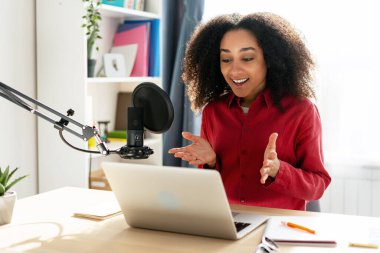 Genç Afrikalı Amerikalı kadın profesyonel mikrofon ve dizüstü bilgisayar kullanarak kendi stüdyosundan podcast kaydediyor. Canlı yayın kavramı
