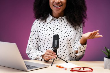 Radyo sunucusu olarak çalışan genç bir kadın. Ev stüdyosunda podcast yaparken mikrofona konuşuyor. Bir dizüstü bilgisayarla çevrili. Not defteri. Ve gözlük. Yaratıcı içerik üretimiyle ilgileniyor.