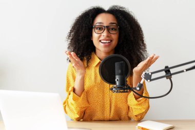Genç gülümseyen Afro-Amerikan kadın şık gözlükler takıyor ve sarı gömlek kendi stüdyosundan podcast yapıyor. Çevrimiçi teknoloji kavramı