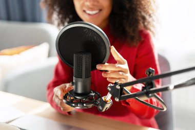 Gülümseyen kadın podcaster profesyonel mikrofonu ayarlarken sıcak ev stüdyosunda seçici bir kayıt oturumuna hazırlanıyor. Profesyonel ekipman konsepti