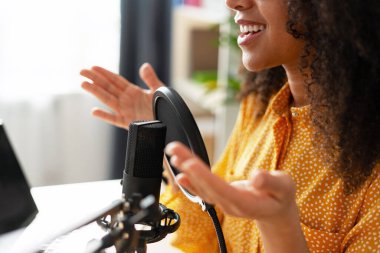 Genç kadın mikrofon ve pop filtresi kullanarak ses podcast 'i kaydediyor, ev stüdyosunda profesyonel mikrofona konuşurken el kol hareketi yapıyor.