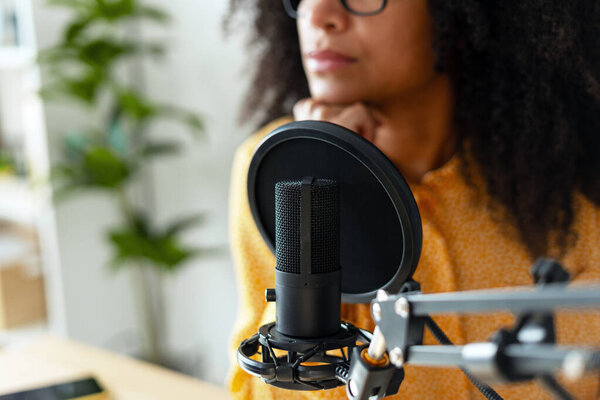 Молодая создательница контента записывает аудио в своей домашней студии, используя профессиональный микрофон с поп-фильтром, обдумывая свои следующие слова. Сосредоточены и погружены в творческий процесс