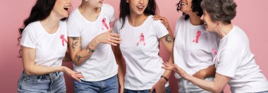 Farklı yaşlarda bir grup kadın beyaz tişörtlere pembe kurdele takıyor, gülüyor ve meme kanseri farkındalığını destekliyor, hastalığa karşı birlikte savaşıyorlar.