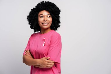 Göğüs kanserini destekleyen kolları çapraz pembe tişört giyen kendine güvenen genç bir kadın.