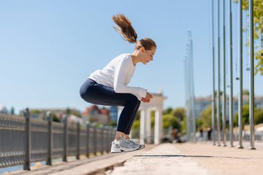 Formda bir kadın, şehir parkında kaldırıma atlayıp sağlıklı yaşam tarzını ve kentsel kondisyonunu teşvik ederek egzersiz yapıyor.