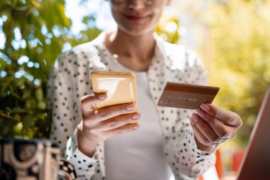 İş kadını elinde kredi kartı tutarken açık havada canlı bir bahçe ortamında internet üzerinden sorunsuz alışveriş yapmak için akıllı telefon kullanıyor.